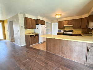 Kitchen with under cabinet range hood, a textured ceiling, a sink, and white appliances
