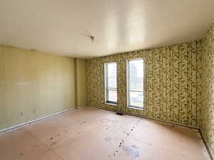 Spare room featuring wallpapered walls, a textured ceiling, and visible vents