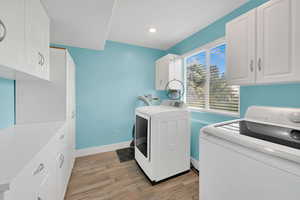 Clothes washing area with washing machine and clothes dryer, light wood-style floors, cabinet space, baseboards, and recessed lighting