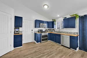 Kitchen with wooden counters, stainless steel appliances, vaulted ceiling, a sink, and blue cabinetry