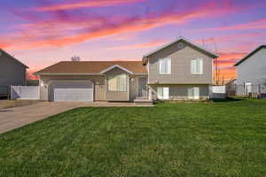 Tri-level home with a yard, an attached garage, concrete driveway, and fence