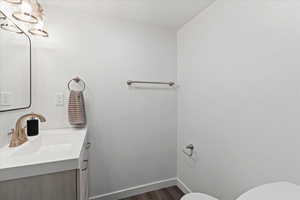 Half bathroom featuring wood finished floors, vanity, baseboards, toilet, and a notable chandelier