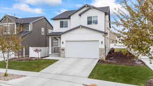 View of front facade with driveway, stone siding, a garage, board and batten siding, and a front yard