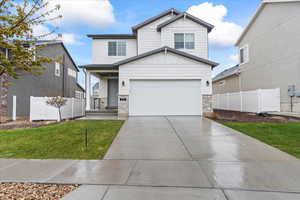 View of front of house featuring fence, board and batten siding, driveway, stone siding, and a garage