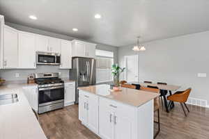 Kitchen with a kitchen breakfast bar, dark wood-style floors, visible vents, white cabinetry, and appliances with stainless steel finishes