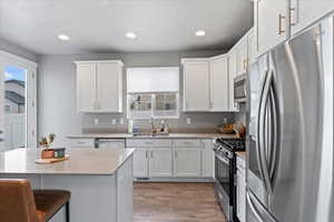 Kitchen with recessed lighting, a sink, light wood-style floors, appliances with stainless steel finishes, and white cabinetry