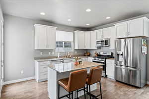 Kitchen featuring a sink, light wood-type flooring, stainless steel appliances, white cabinetry, and recessed lighting