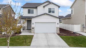 View of front of home with an attached garage, stone siding, a front yard, and fence