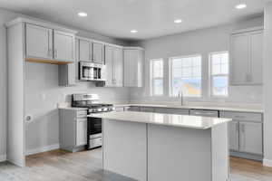 Kitchen with appliances with stainless steel finishes, light wood-style flooring, a sink, and light countertops