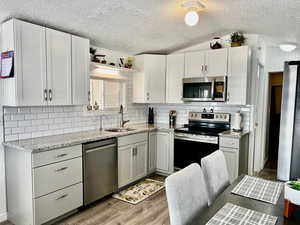 Kitchen with tasteful backsplash, a sink, a textured ceiling, light wood finished floors, and appliances with stainless steel finishes
