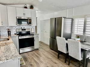 Kitchen with a textured ceiling, tasteful backsplash, light wood-style floors, light stone countertops, and appliances with stainless steel finishes