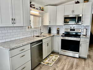 Kitchen featuring decorative backsplash, stainless steel appliances, a sink, and a textured ceiling