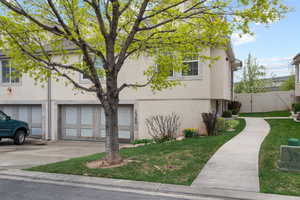 View of side of home featuring driveway, an attached garage, fence, a yard, and stucco siding