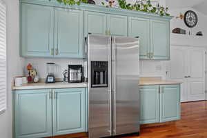 Kitchen with blue cabinetry, stainless steel fridge with ice dispenser, wood finished floors, and light countertops