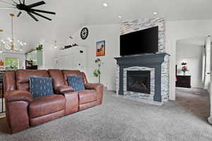 Living room featuring vaulted ceiling, ceiling fan with notable chandelier, carpet, a fireplace, and recessed lighting