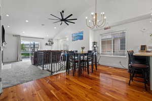 Dining space with baseboards, recessed lighting, ceiling fan with notable chandelier, hardwood / wood-style floors, and high vaulted ceiling
