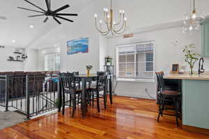 Dining area featuring high vaulted ceiling, wood finished floors, ceiling fan with notable chandelier, baseboards, and recessed lighting