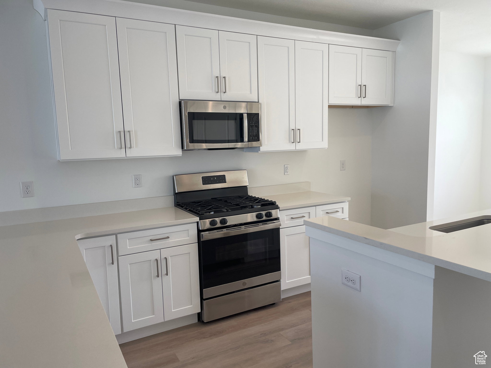 Kitchen with white cabinets, appliances with stainless steel finishes, light wood-style floors, and light countertops