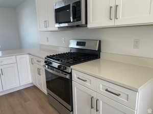 Kitchen with white cabinets, light countertops, wood finished floors, and appliances with stainless steel finishes