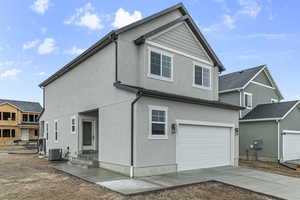 Rear view of house with concrete driveway, central AC unit, stucco siding, and a garage