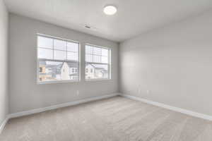 Carpeted empty room featuring a textured ceiling, visible vents, and baseboards