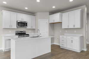 Kitchen with stainless steel appliances, wood finished floors, a sink, baseboards, and white cabinetry