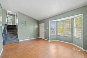 Unfurnished living room with lofted ceiling, stairway, visible vents, light wood-style floors, and baseboards