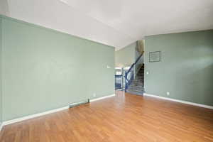 Unfurnished room featuring light wood-type flooring, lofted ceiling, baseboards, and stairway
