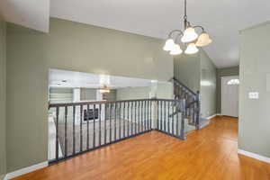 Interior space with ceiling fan with notable chandelier, baseboards, vaulted ceiling, and wood finished floors