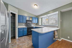Kitchen with a sink, blue cabinets, black appliances, light countertops, and a peninsula