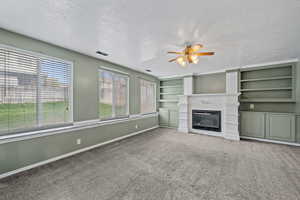 Unfurnished living room with baseboards, a ceiling fan, a glass covered fireplace, and a textured ceiling