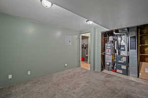 Finished below grade area featuring a textured ceiling, carpet floors, gas water heater, and heating unit