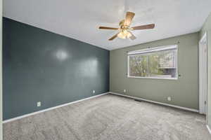 Spare room featuring visible vents, carpet floors, baseboards, a textured ceiling, and ceiling fan