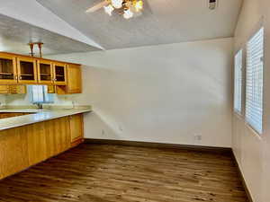 Kitchen with brown cabinets, lofted ceiling, dark wood-style floors, light countertops, and a ceiling fan