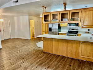 Kitchen with appliances with stainless steel finishes, light countertops, a peninsula, wood finished floors, and glass insert cabinets