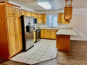 Kitchen with stainless steel appliances, a peninsula, light countertops, light wood-type flooring, and a textured ceiling