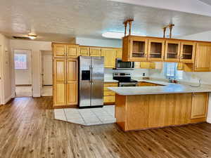 Kitchen featuring appliances with stainless steel finishes, a peninsula, light wood-style floors, light countertops, and glass insert cabinets
