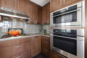 Kitchen featuring backsplash, under cabinet range hood, and appliances with stainless steel finishes