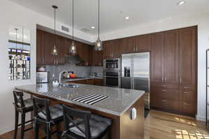Kitchen with decorative backsplash, under cabinet range hood, stainless steel appliances, and light wood-type flooring