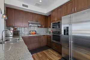 Kitchen featuring a sink, stainless steel appliances, under cabinet range hood, light stone countertops