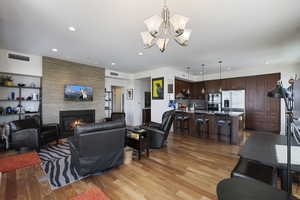 Living area featuring a stone fireplace, a chandelier, light wood finished floors, visible vents, and recessed lighting