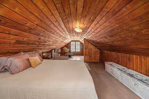 Unfurnished bedroom with wooden walls, dark wood-style floors, vaulted ceiling, and wooden ceiling