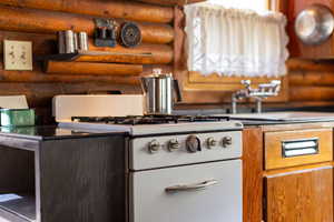 Kitchen with brown cabinets, white gas stove, a sink, and rustic walls
