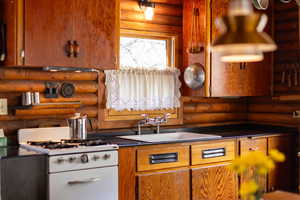 Kitchen with a sink, rustic walls, dark countertops, brown cabinetry, and cooktop