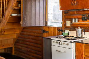 Kitchen featuring brown cabinets, log walls, and white range with gas stovetop