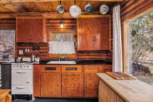 Kitchen featuring brown cabinetry, wooden ceiling, rustic walls, and a sink
