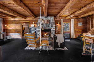 Living area featuring a stone fireplace, beam ceiling, log walls, and wood ceiling