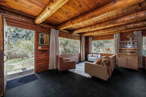 Living room with wood ceiling, beam ceiling, rustic walls, and a healthy amount of sunlight
