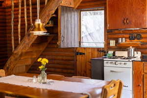 Kitchen with rustic walls, brown cabinets, open shelves, dark countertops, and white range with gas stovetop