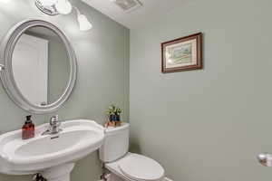 Half bathroom featuring visible vents, toilet, baseboards, and a sink